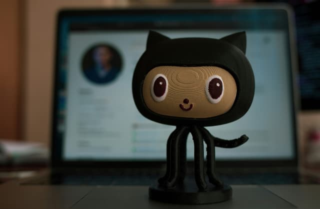 The Octocat GitHub mascot on a desk with the website in the background